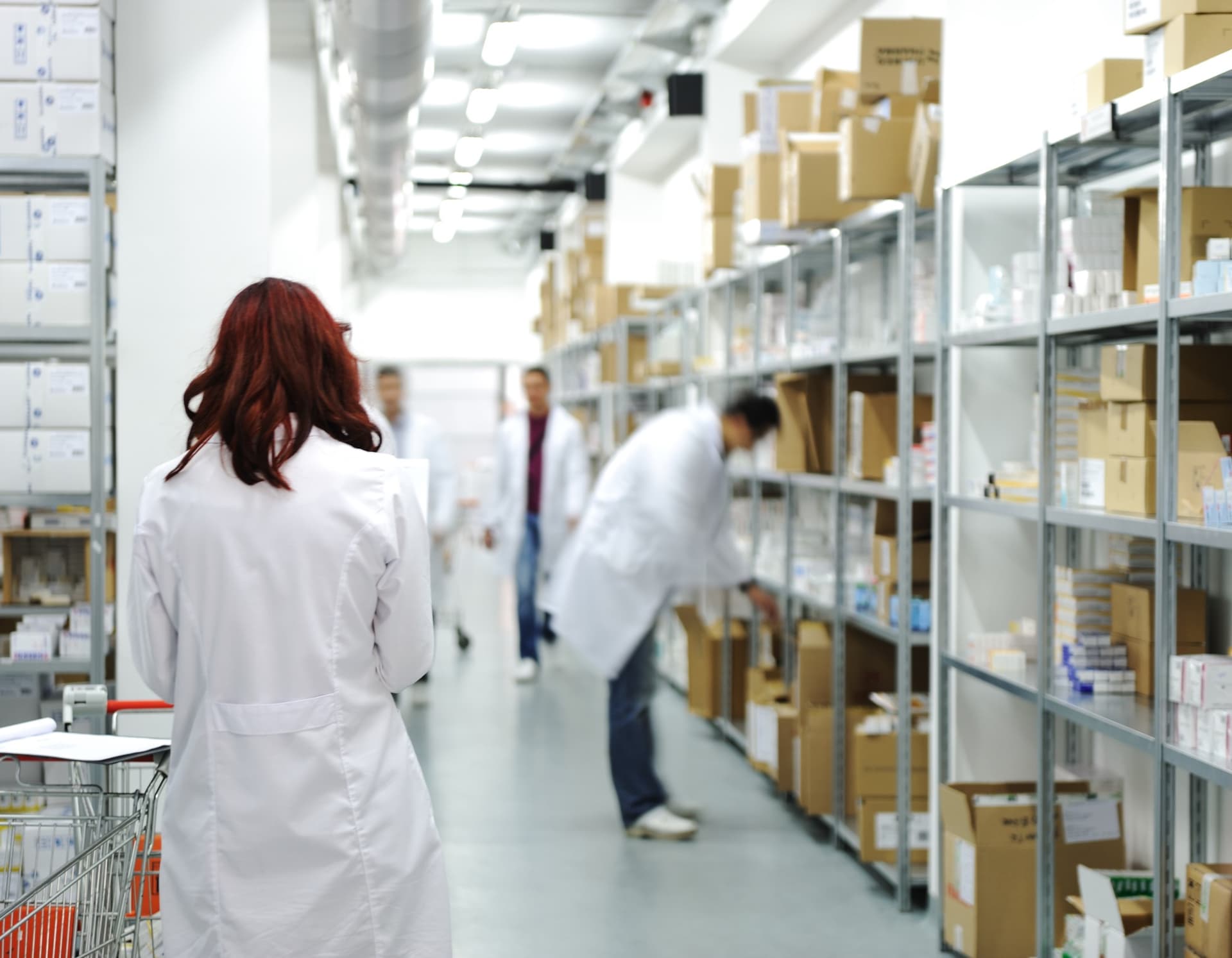 Staff in lab coats checking stock on pharmacy shelves