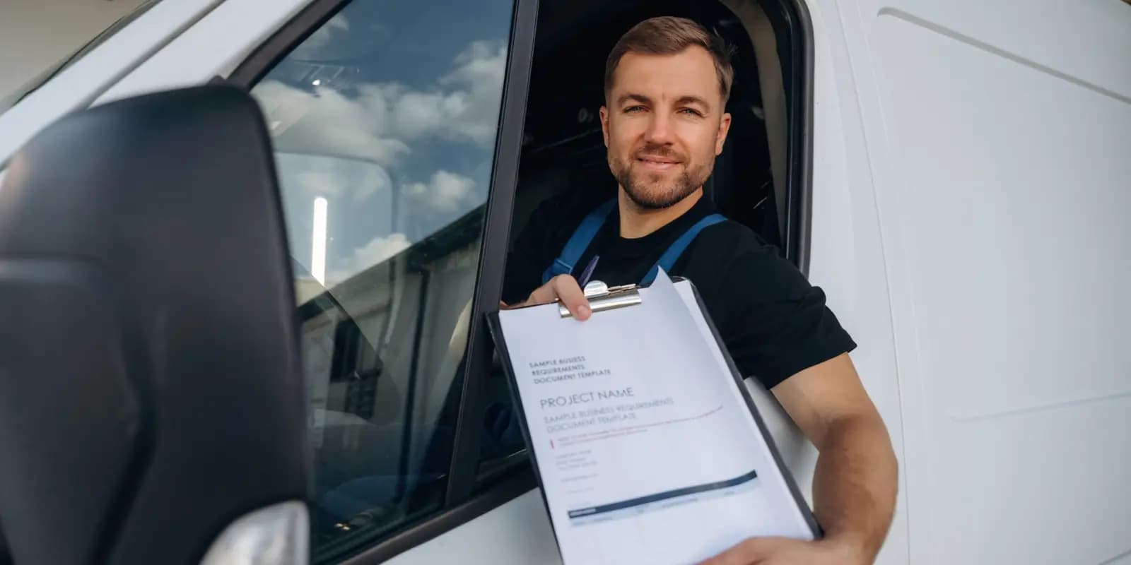 Driver leaning out of a work van window, handing over paperwork on a clipboard