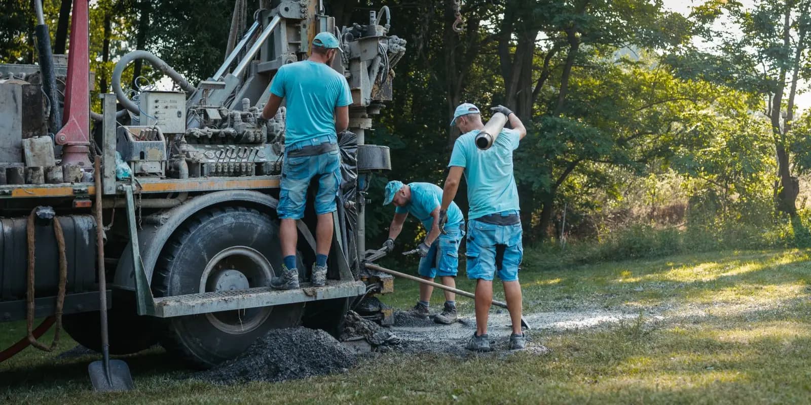 Three-person field crew working beside a truck-mounted drill rig on a grassy site